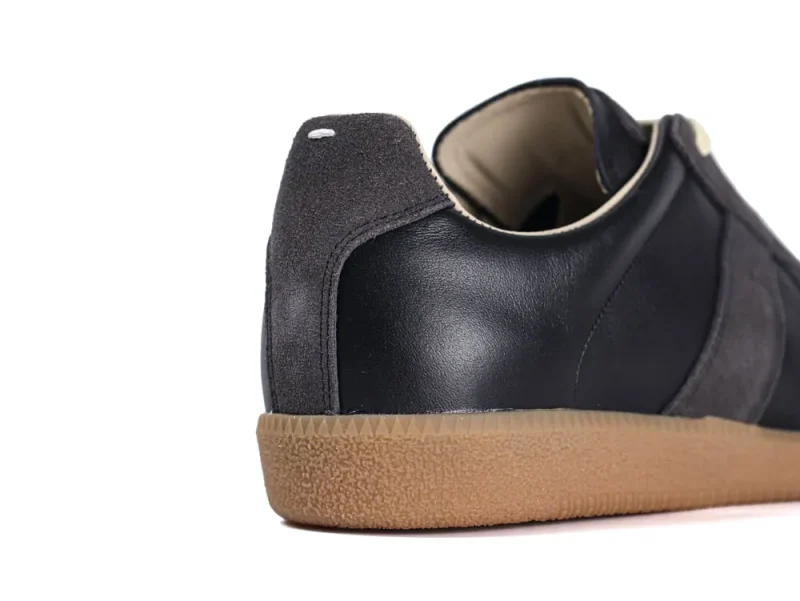 Black leather sneaker with suede detailing and beige rubber sole, rear view.