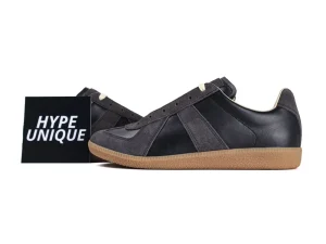 Black leather sneaker with gray suede accents and brown rubber sole, side view.
