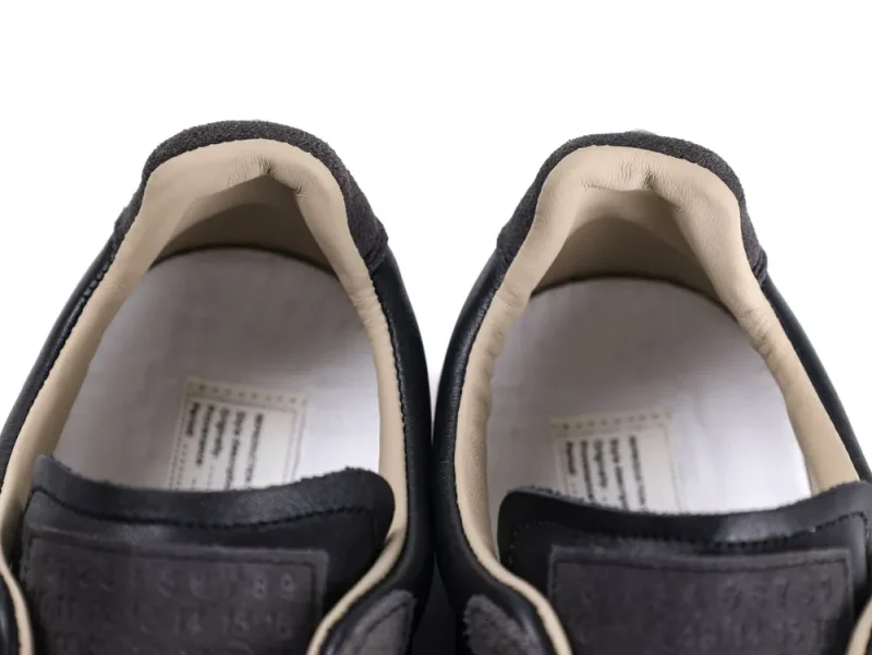 Black leather sneakers with beige suede lining, focusing on the interior heel area.