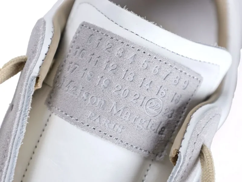 White and gray shoe tongue with embossed suede label and beige laces.