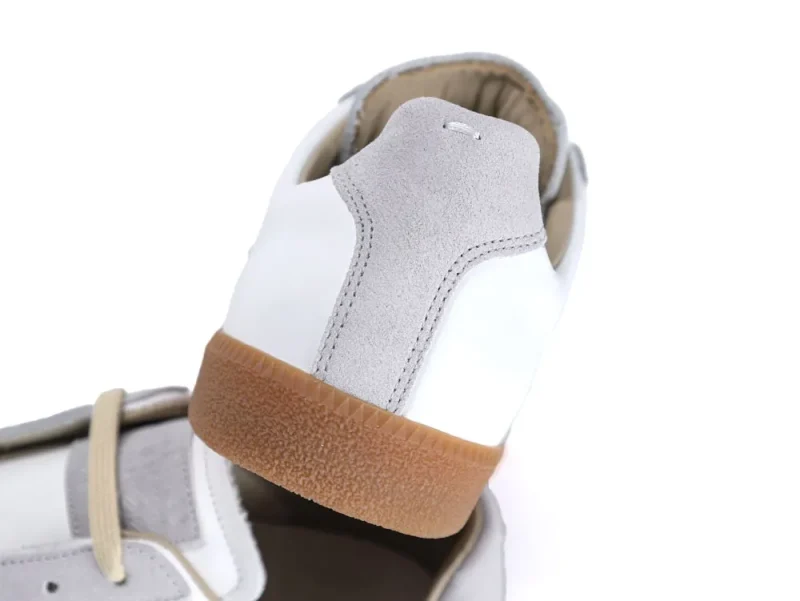 White leather sneaker with gray suede accents and brown rubber sole.