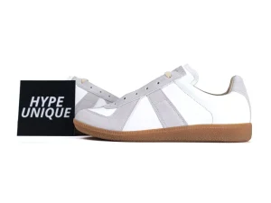White and gray suede sneakers with brown rubber sole, displayed beside branding card.