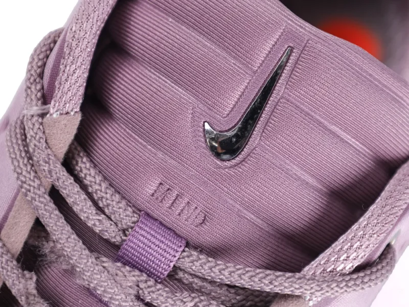 Close-up of a purple fabric shoe tongue with a metallic logo and laces.