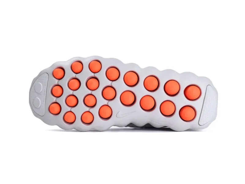 Gray shoe sole with orange circular rubber grips, featuring textured and smooth surfaces.