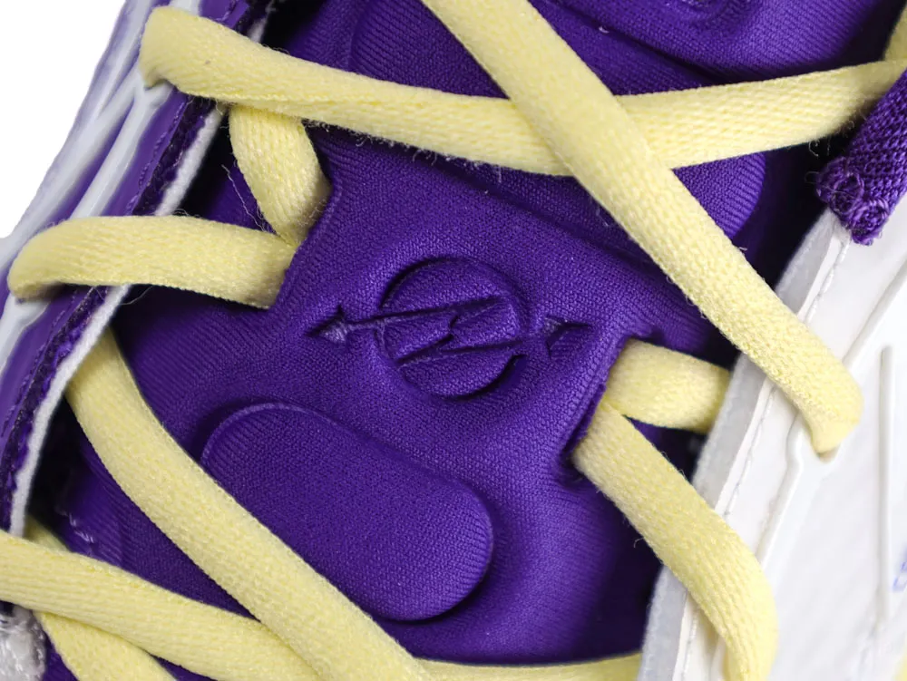 Close-up of a purple fabric sneaker with yellow laces and embossed logo detail.