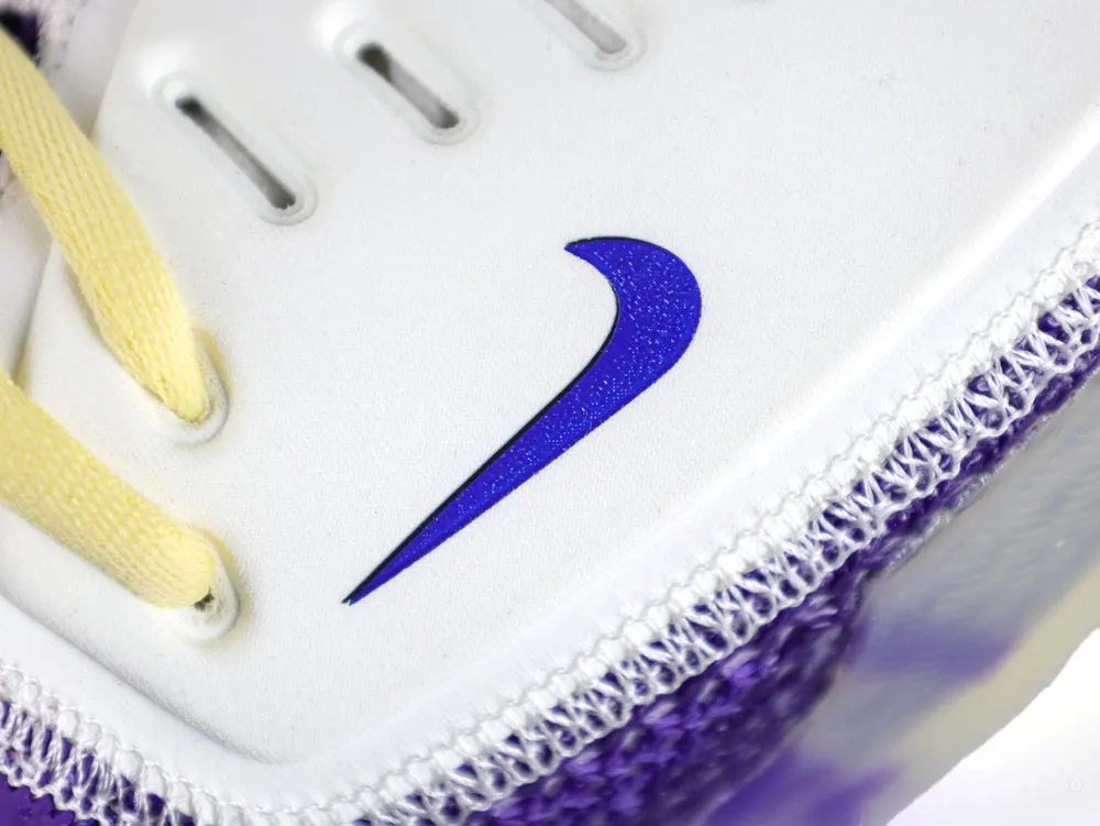 Close-up of a white and purple sneaker with yellow laces and mesh detailing.