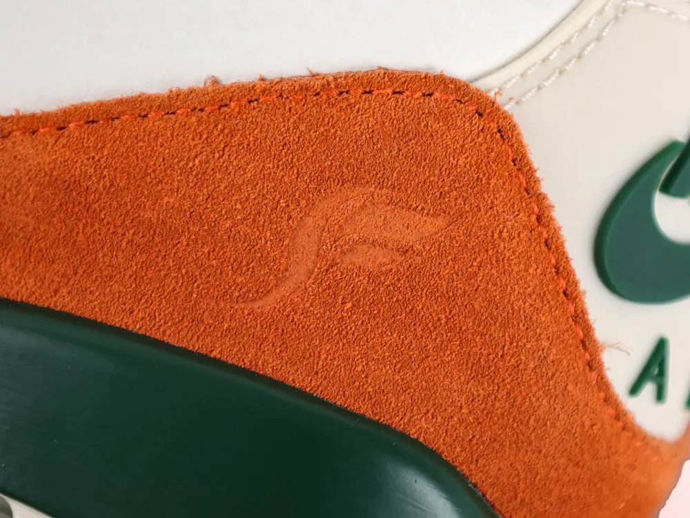 Close-up of an orange suede sneaker with green details and stitching.