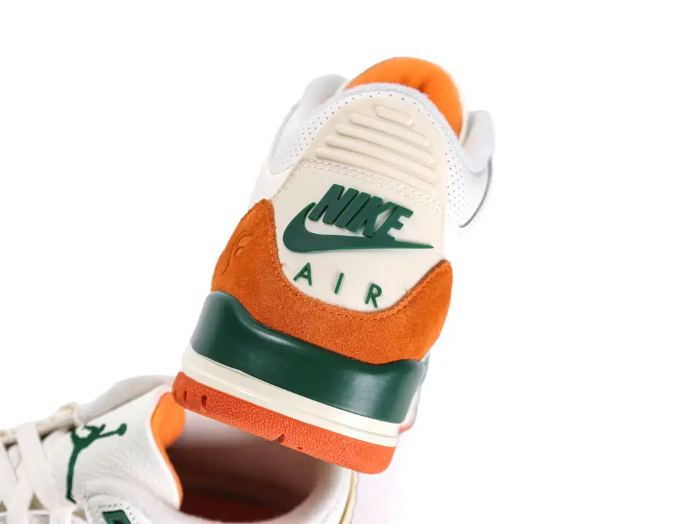 White leather sneaker with orange suede accents and green rubber details.