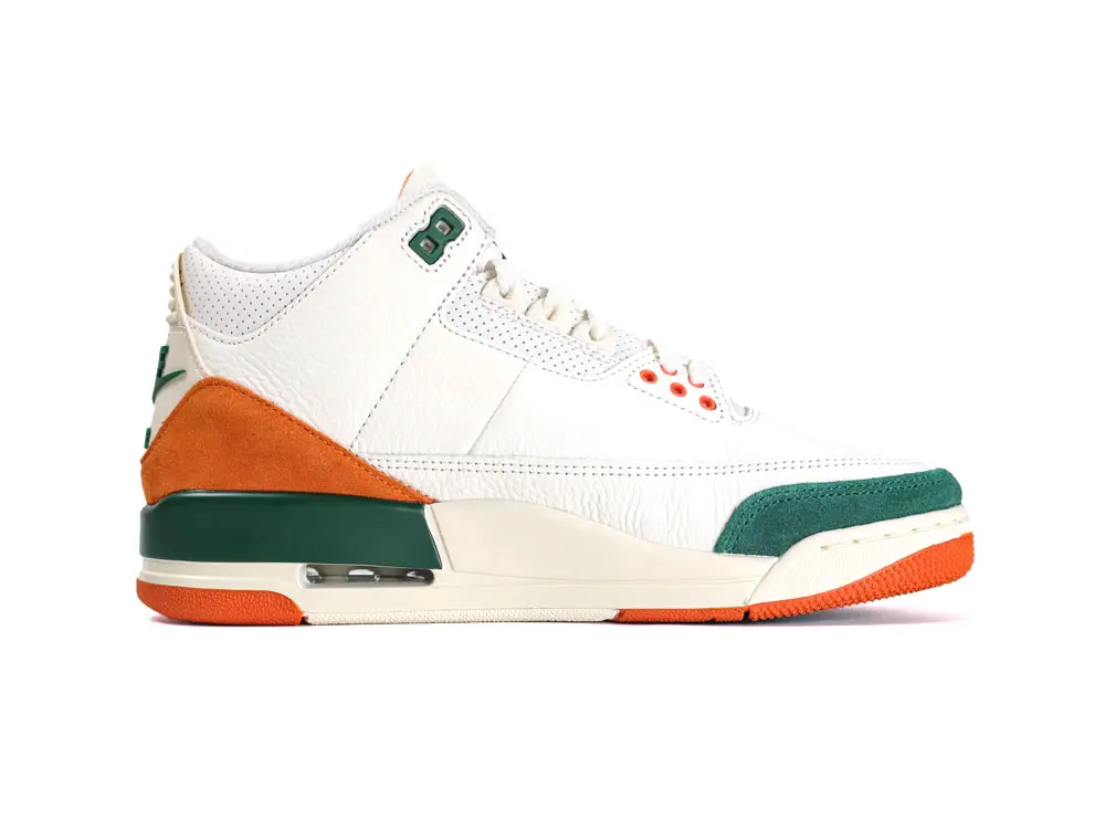 White leather sneaker with orange suede accents and green details on sole.