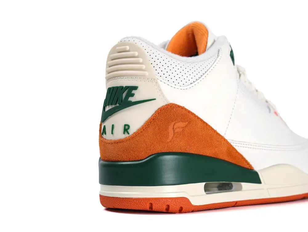 White leather sneaker with orange suede accents and green rubber heel detailing.