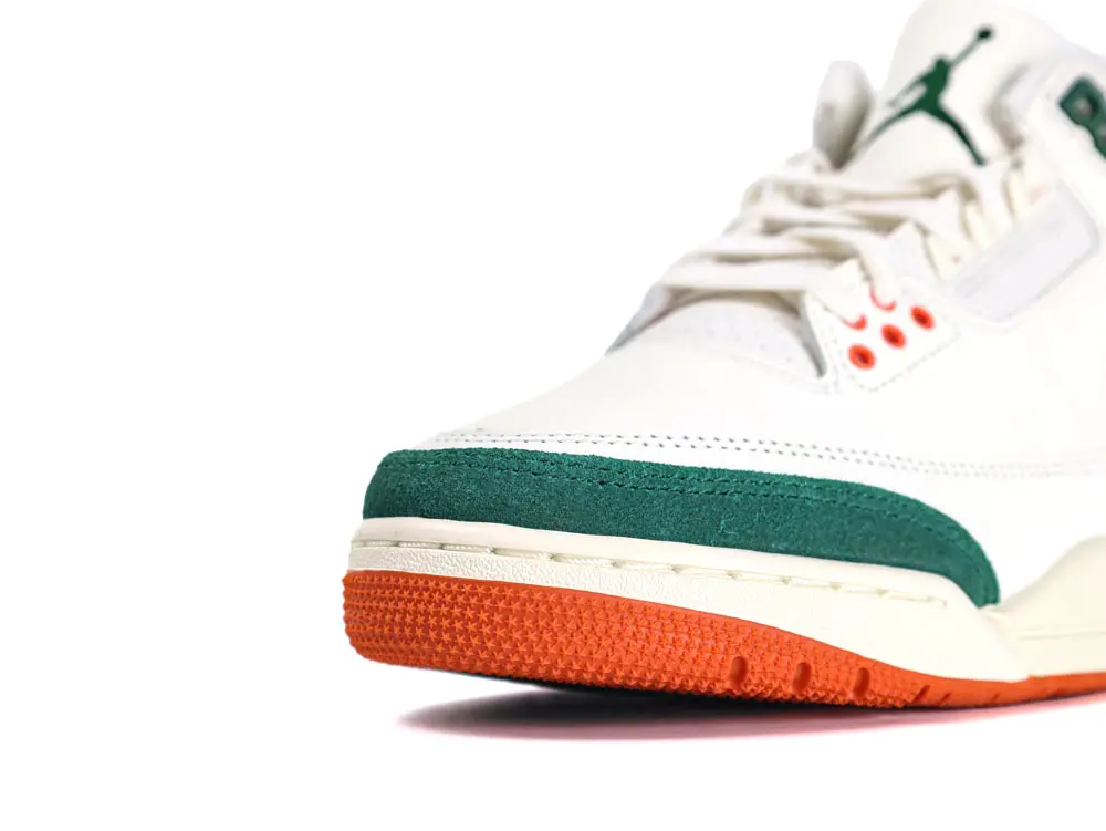 White sneaker with green suede accent and orange rubber outsole, featuring laces and eyelets.