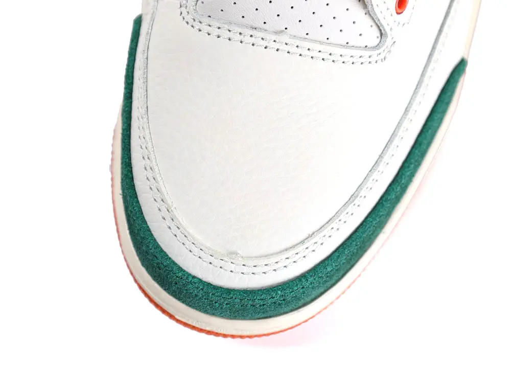 White leather shoe with green suede trim and perforated details near the toe.