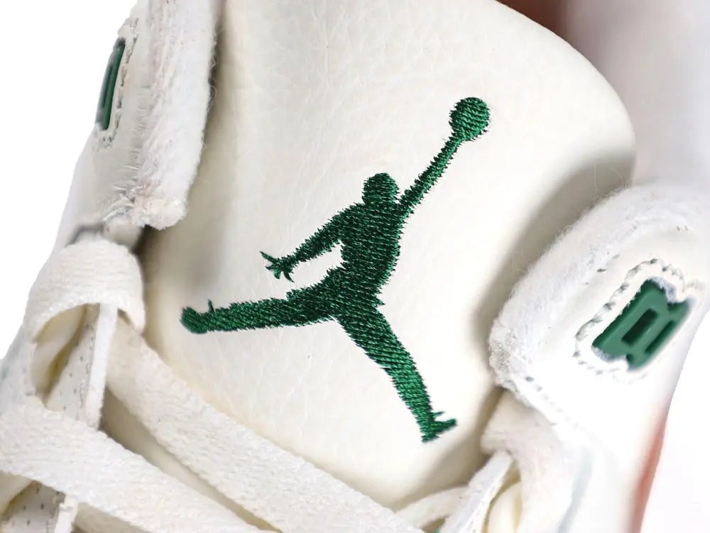 Close-up of white leather shoe tongue with green embroidered logo and lace details.