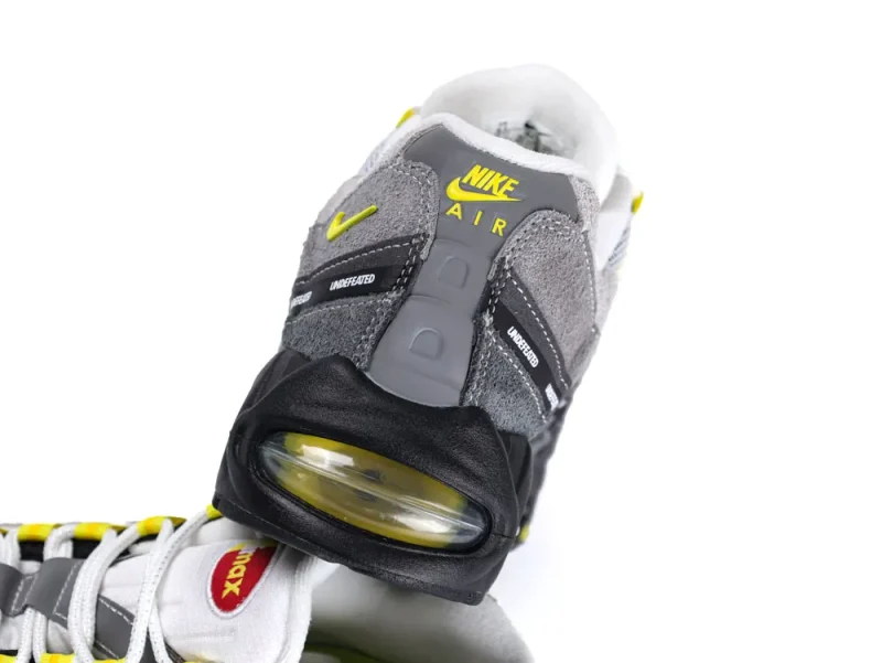 Gray and black sneaker with suede and leather, featuring yellow accents and air cushion.