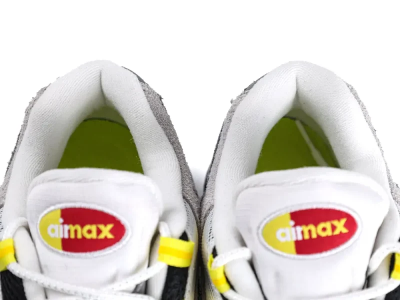 Close-up of white and gray sneakers with yellow accents and branded tongue logo.