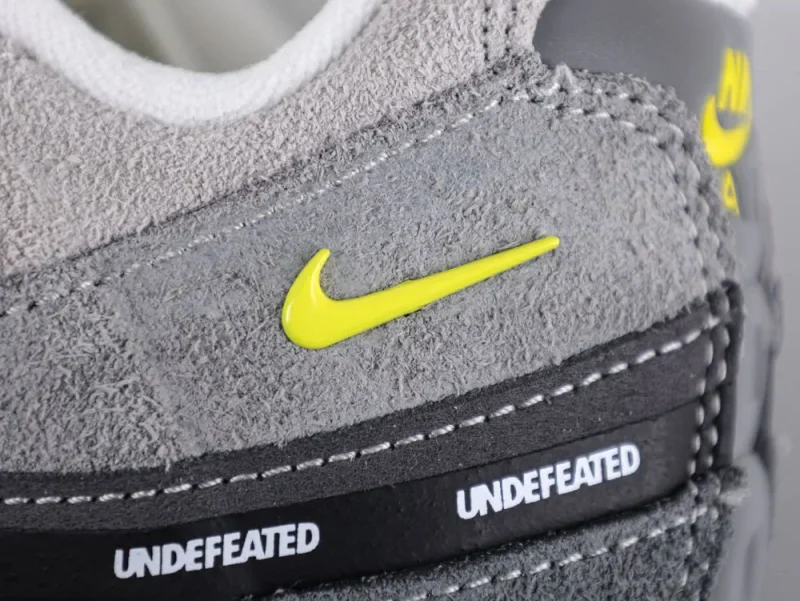 Close-up of gray suede sneaker with yellow logo and black leather stripe detail.