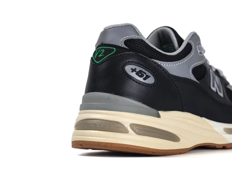 Black and gray leather sneaker heel with green detailing on a beige sole.