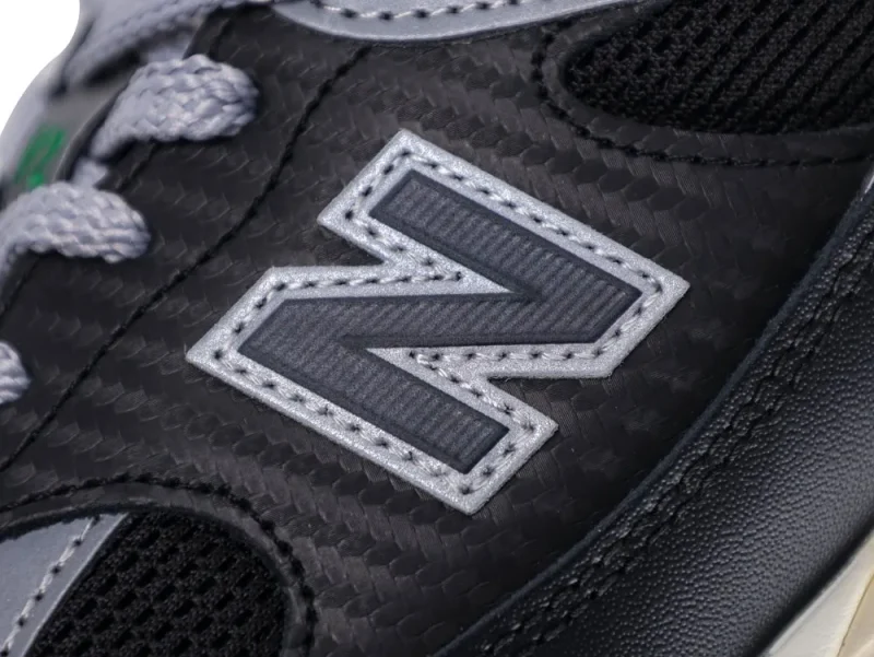 Close-up of black synthetic sneaker with gray fabric logo and textured material.