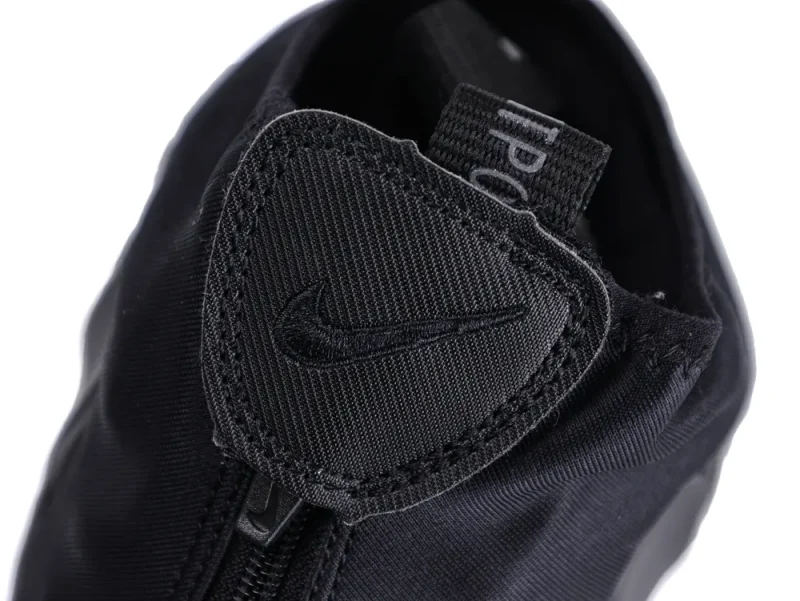 Close-up of a black fabric shoe with a zipper and stitched logo.