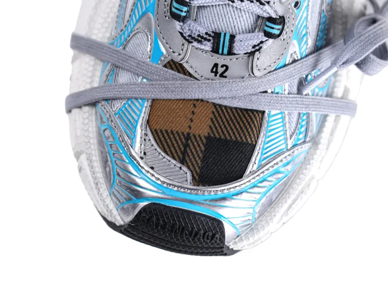 Close-up of a sneaker's front with blue, silver, and plaid fabric detailing.