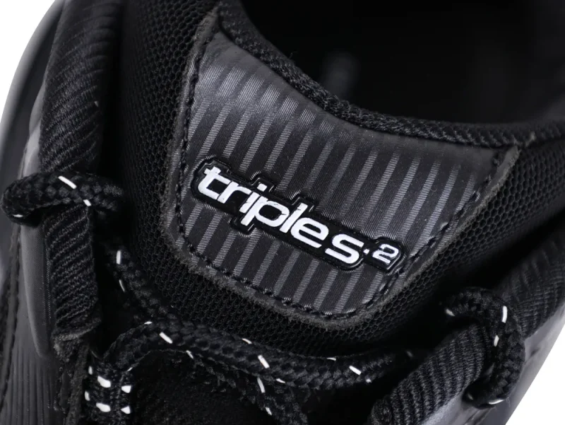 Close-up of black shoe tongue featuring textured material and white "triples" logo.