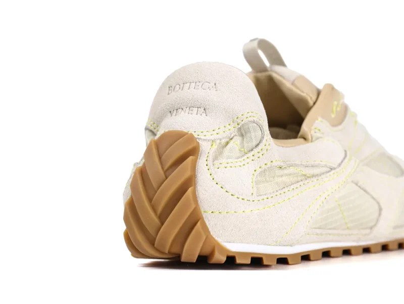 Cream suede sneaker with gum sole, featuring intricate stitching details at heel.