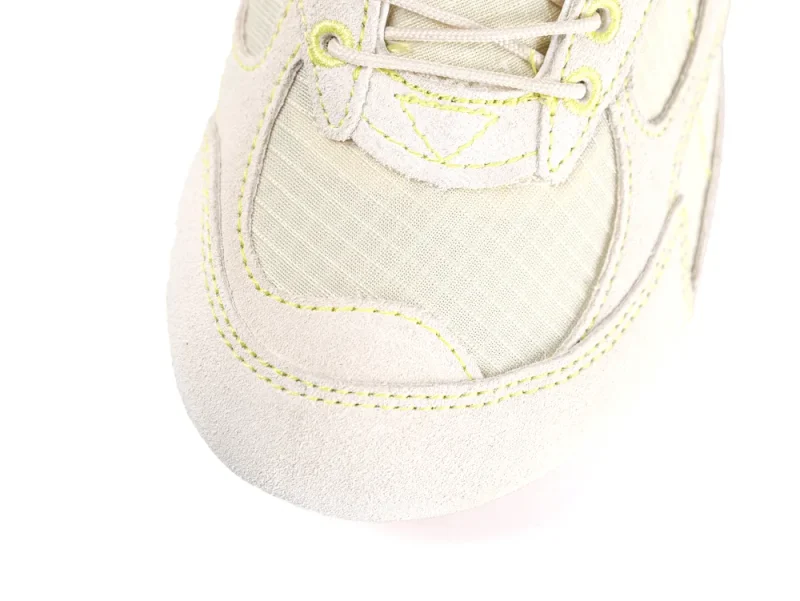 Close-up of beige suede and fabric sneaker toe with yellow stitching details.
