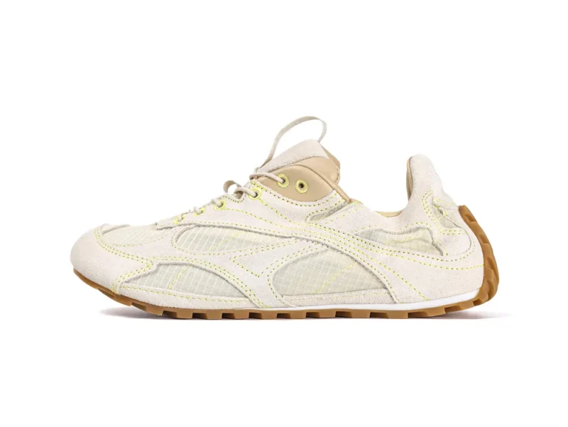 Beige and tan sneaker with textile upper and rubber sole, featuring yellow stitching.