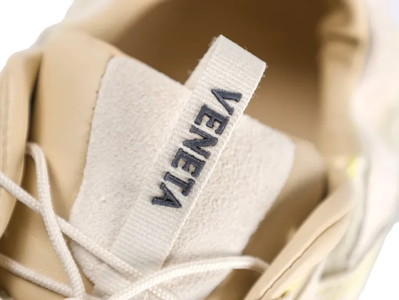 Beige sneaker with suede material and fabric pull tab featuring stitched text.