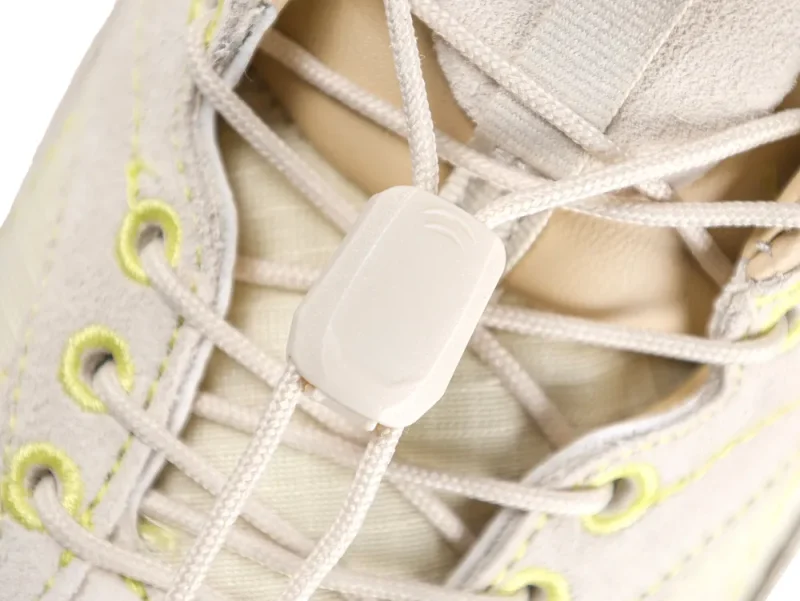 Close-up of beige suede shoe with laces intertwined through neon-accented eyelets.
