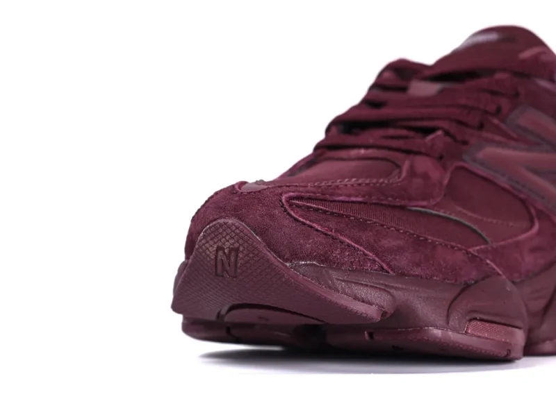 Close-up of a maroon suede sneaker's toe, showcasing detailed stitching and texture.