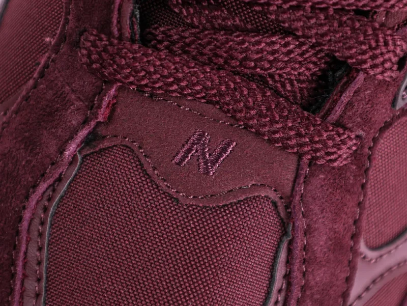 Close-up of a burgundy sneaker, showcasing fabric and suede material with laces.
