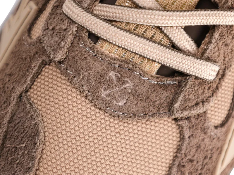 Close-up of beige and brown suede sneaker with textured fabric and laces.