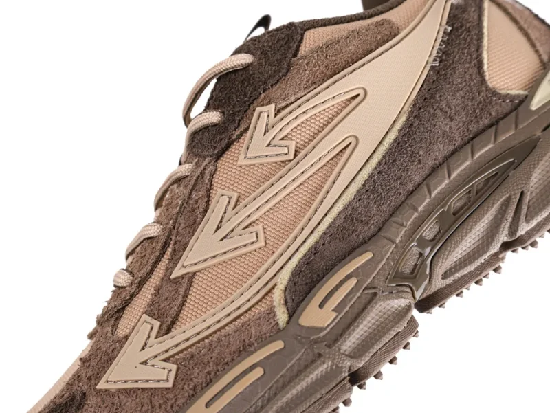 Close-up of a brown suede and fabric sneaker with arrow design details.