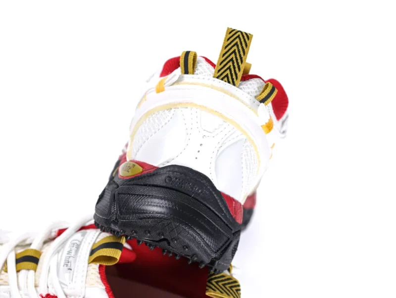 White leather sneaker with black sole, red accents, and yellow pull tab.