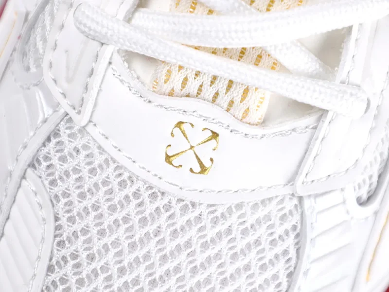 White sneaker with gold logo, featuring mesh and leather materials on the upper.