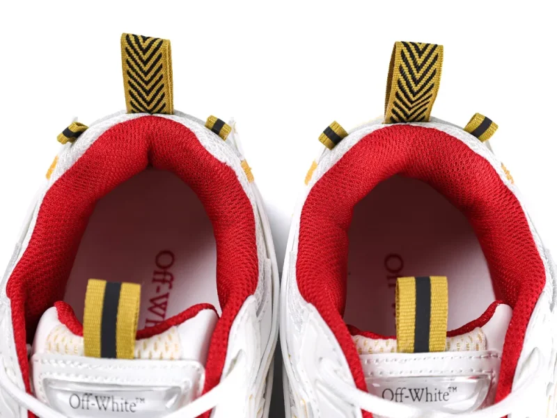 White sneakers with red fabric lining and yellow pull tabs featuring black stripes.