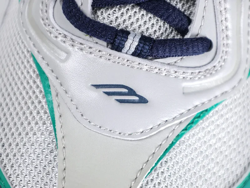 Close-up of the grey leather tongue featuring a dark blue embossed "B" logo and navy blue laces.