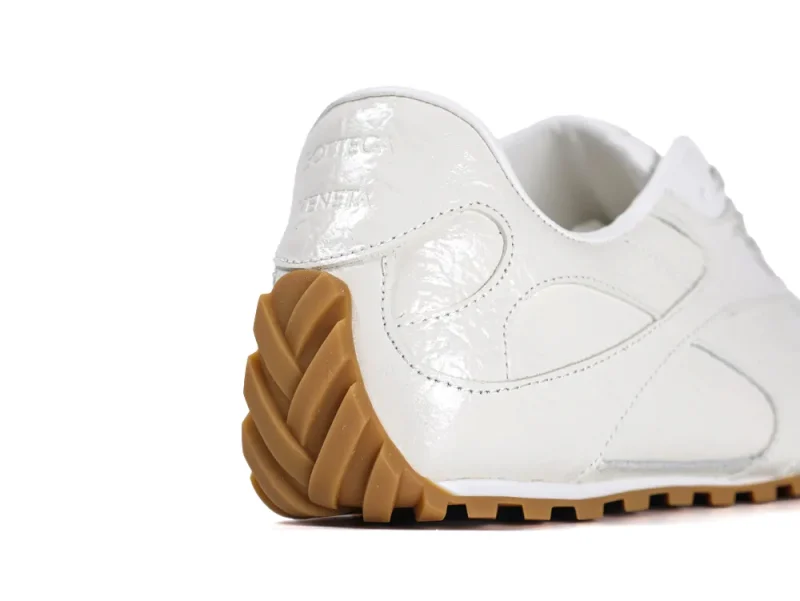 Rear angle of the sneaker highlighting the shiny cream leather finish and textured gum rubber heel