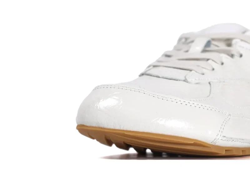 Close-up of the rounded toe on cream patent leather Orbit Flash sneakers with a gum outsole.