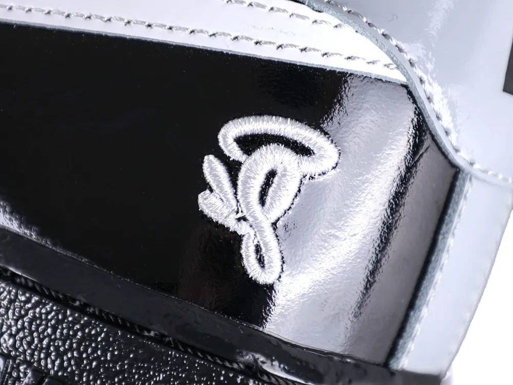Close-up of the white embroidered Syna World "C" logo on the black patent leather heel.