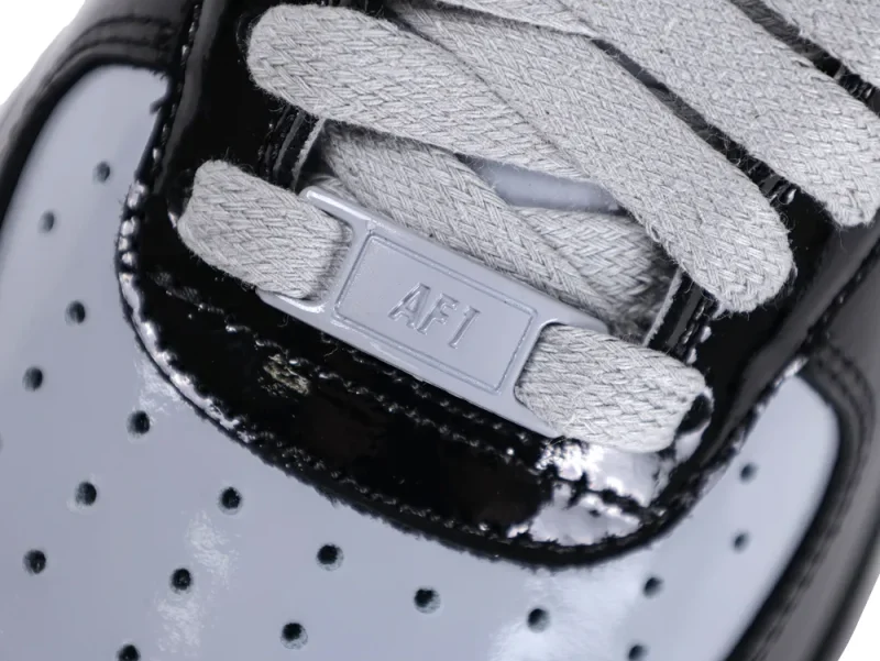 Close-up of the grey "AF1" lace dubrae and flat grey laces on the black patent leather upper.