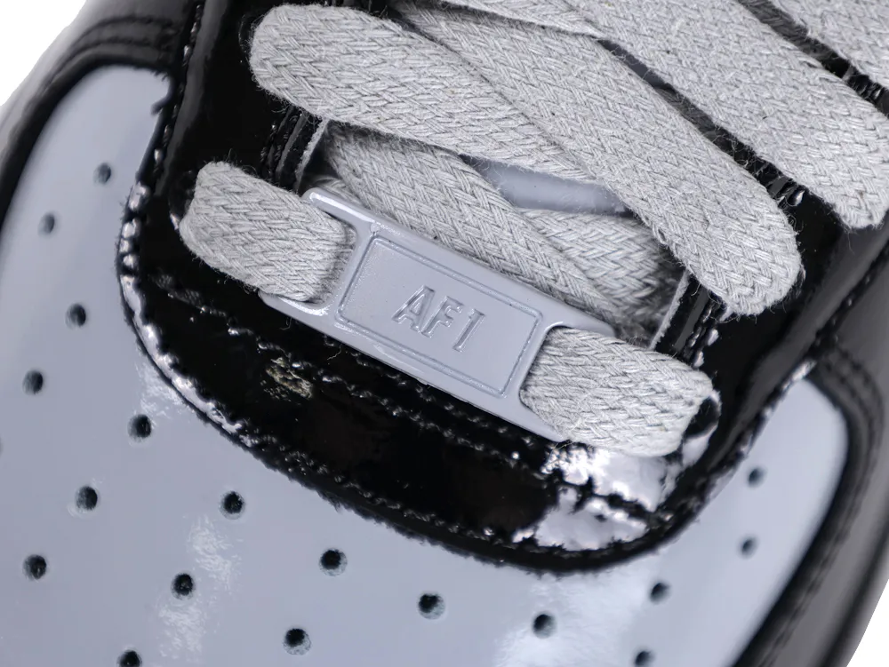Close-up of the grey "AF1" lace dubrae and flat grey laces on the black patent leather upper.
