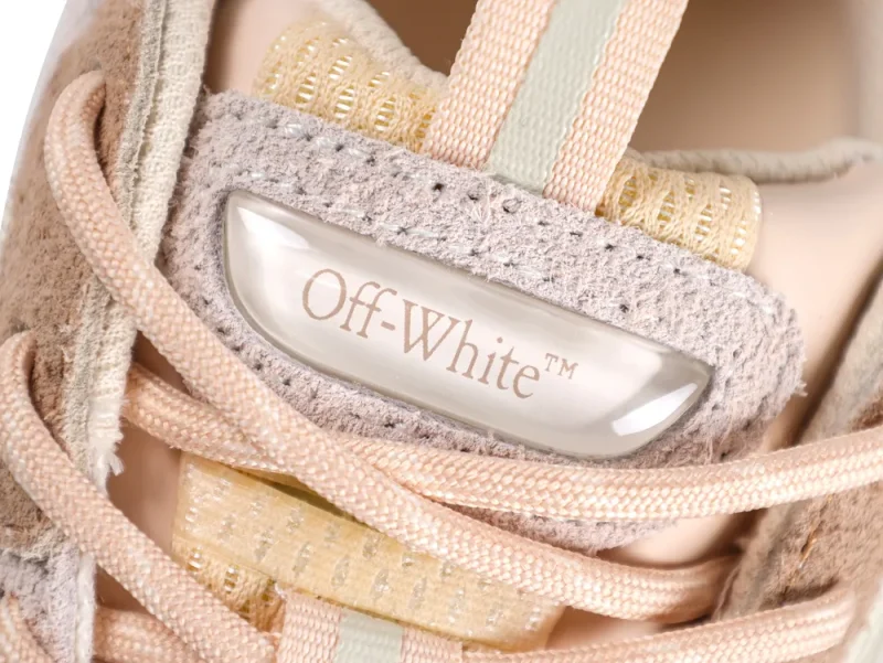 Close-up of the sneaker tongue featuring a glossy, translucent Off-White logo badge set against beige suede.