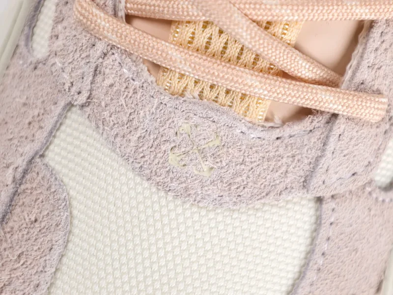 Close-up of the light pink laces and an embroidered arrow logo on the beige suede.